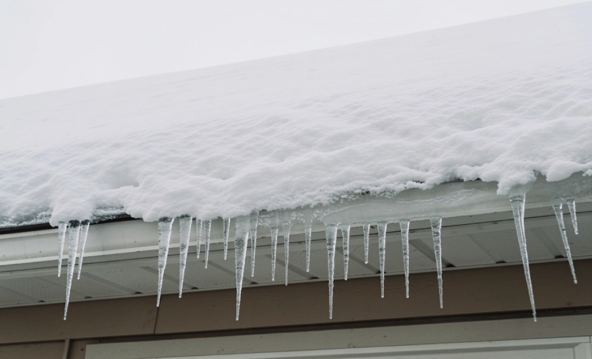 Ice dam forming along the eaves of a residential roof with icicles and accumulated snow
